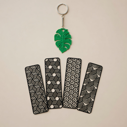 Set of four black patterned keychains with a green leaf-shaped keychain on a beige background