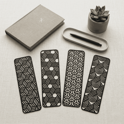 Four black geometric patterned bookmarks on a light surface with a notebook and pen.