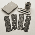 Four black geometric patterned bookmarks on a light surface with a notebook and pen.